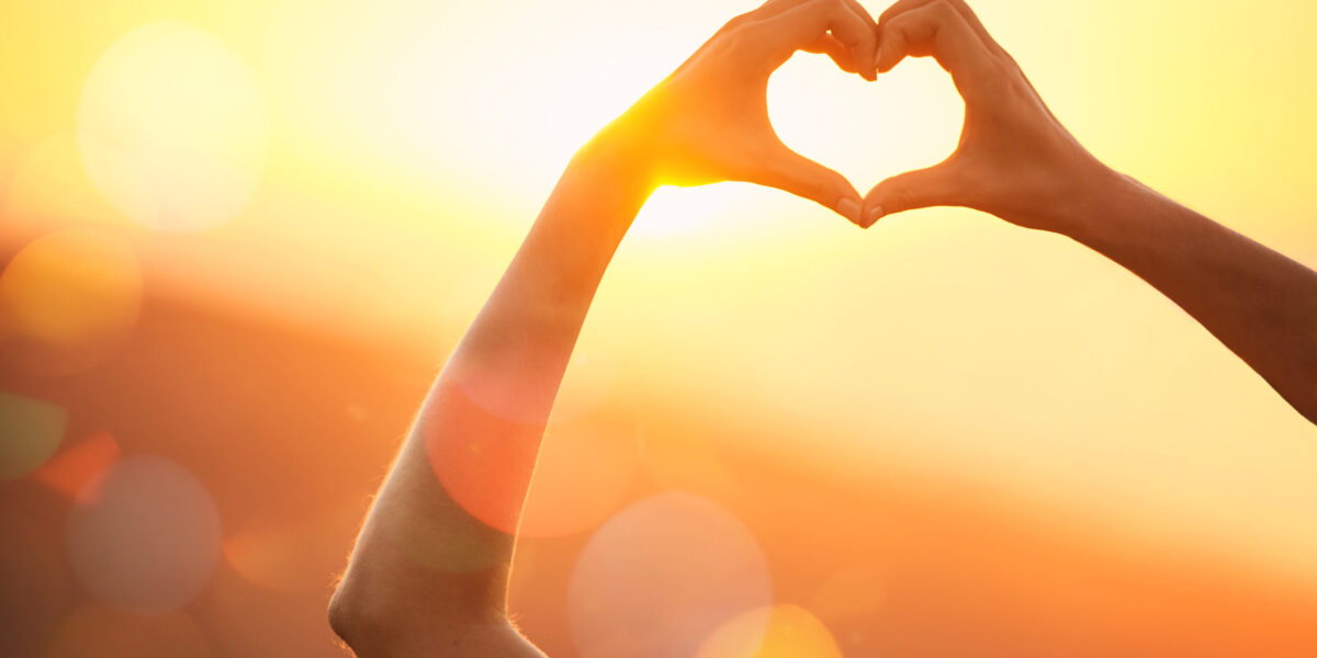 Shot of an unidentifiable womans hands making a heart shape over a sunset landscape