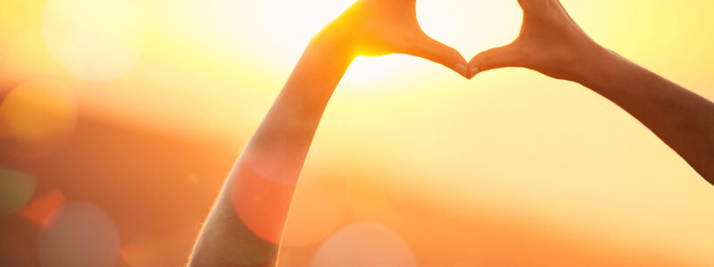 Shot of an unidentifiable womans hands making a heart shape over a sunset landscape