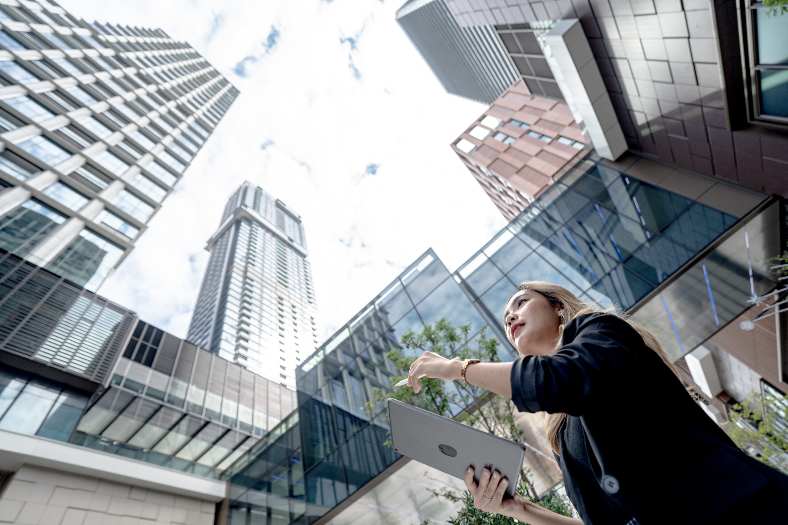 professional woman working on a tablet outdoors, surrounded by lush greenery and city skyscrapers. A symbol of remote work, innovation, and a balanced urban lifestyle