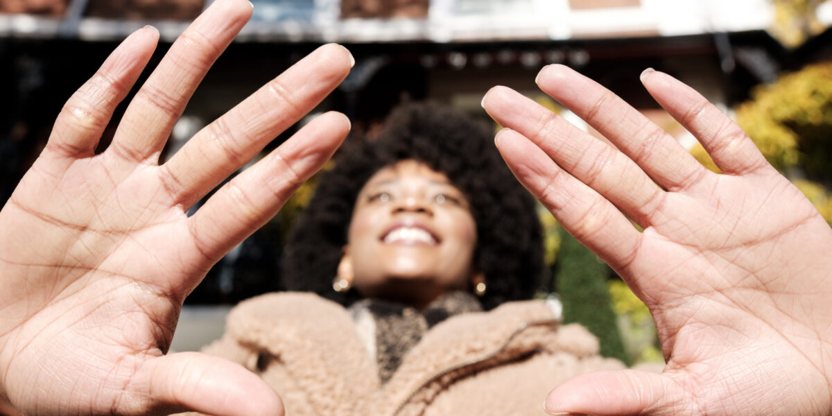 Close-up of palm of hands of young woman in the street. Only the hands are in focus, her face is blurry. It is a cold winter day and she is wearing a thick coat and scarf