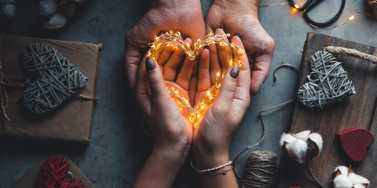 Top view of male and female hands holding red gift box with golden ribbon on pink background Flat lay.