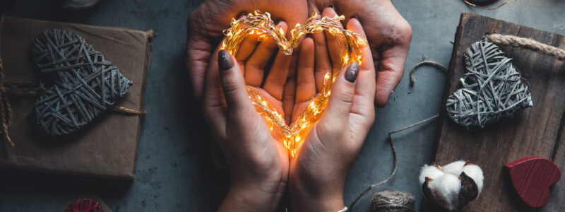 Top view of male and female hands holding red gift box with golden ribbon on pink background Flat lay.
