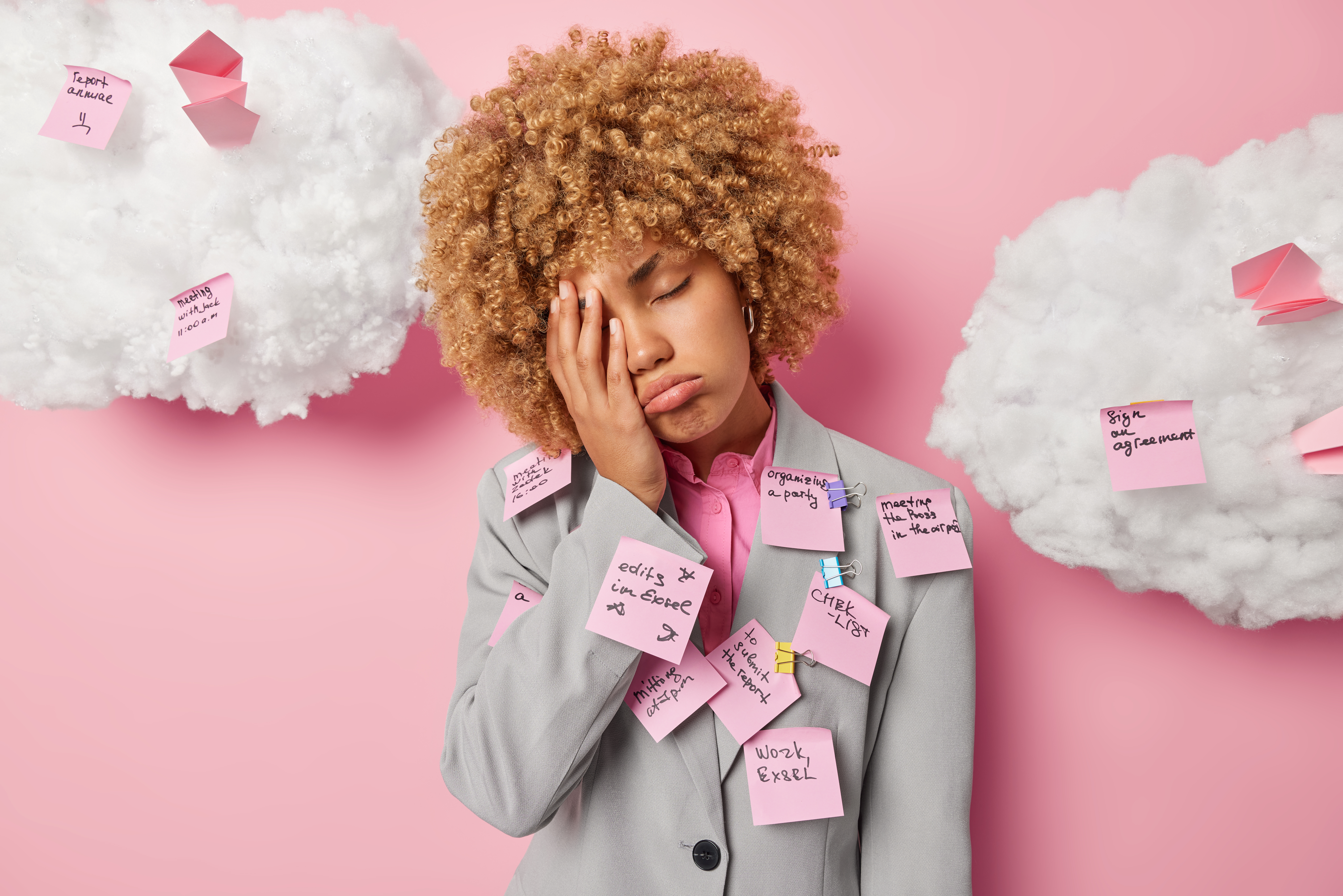 Photo of curly haired woman covers half of face feels tired and exhausted dressed formally covered with stickers with list to do isolated over pink wall white clouds overhead